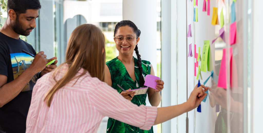 Group of young people putting post it notes onto a whiteboard in a workshop